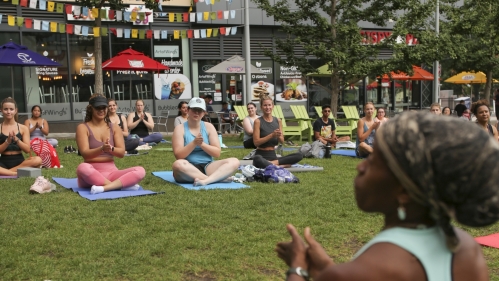 Students and an instructor sit cross-legged in the grass at the end of an outdoor yoga session at Rutgers