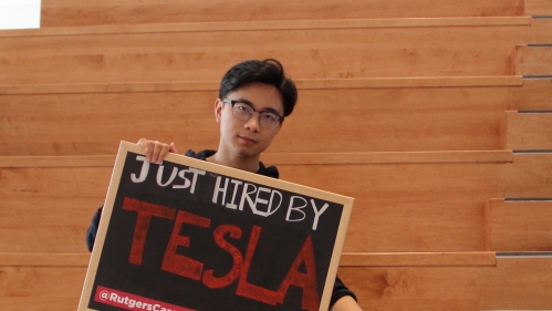 A student holds up a sign after she is hired by Tesla