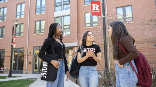 Three students chat outside on the College Avenue campus in front of a dorm.