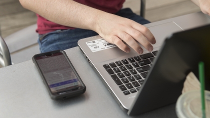 A student types on a laptop next to a cell phone
