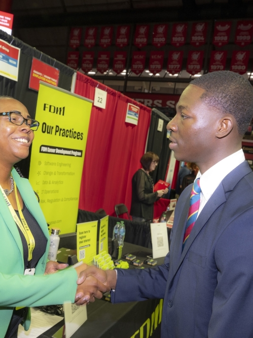 Potential employer and student shaking hands at a booth at the Career and Internship Fair