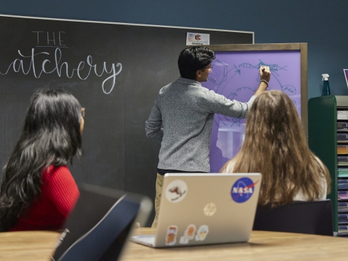 Two students watching another write on a dry erase board in The Hatchery at Alexander Library