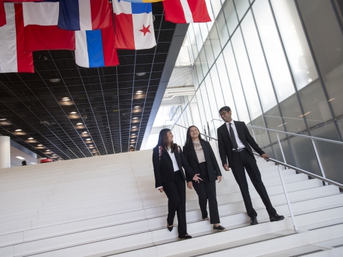 Three students in business attire walking down white steps