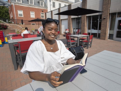 A student reads a book at a table on a patio at the Douglass Student Center