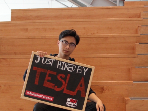 A student holds up a sign after she is hired by Tesla