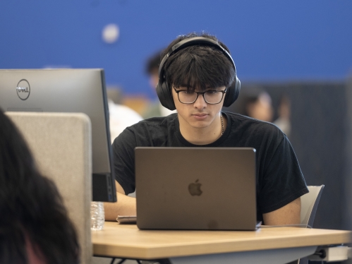 A student wearing headphones works on a laptop in the library